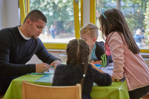 Ein Erzieher malt mit drei Kindern an einem Tisch